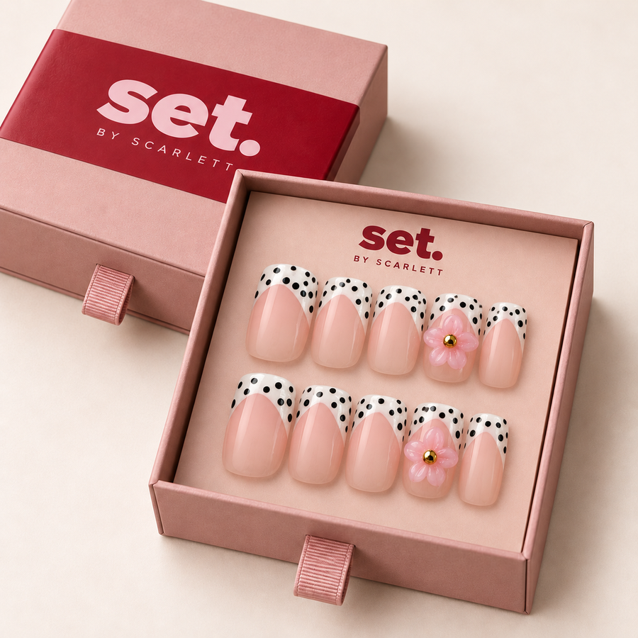Dotty Petal: Black-spotted white French tips, raised pink flowers and gold-tone centres. Digitally styled packaging mockup based on Scarlett's photographed nail set.